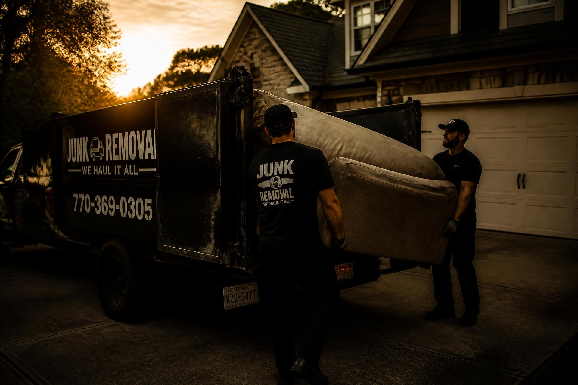 Junk removal crew loading an old couch into a truck at sunset